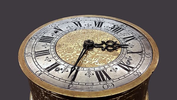 An old table clock standing on a flat surface with its dial facing forward