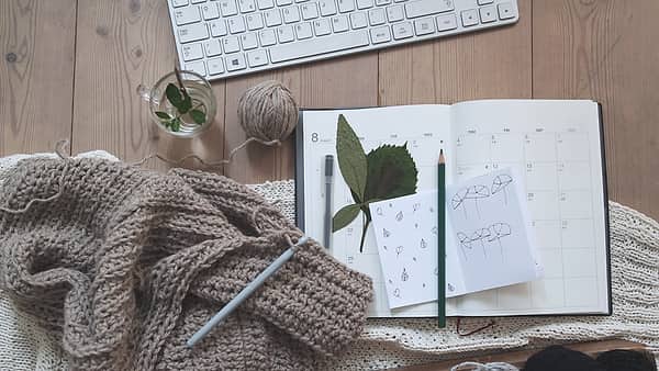 An open paper planner on a desk beside a keyboard, its dated pages marked in pencil