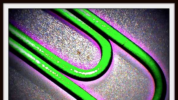 A single metal paper clip photographed in close-up against a plain pale background