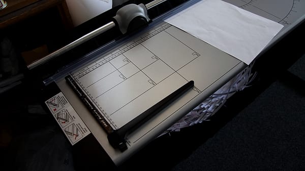 A large format paper trimmer on a work surface with its blade arm raised