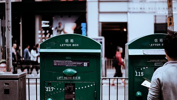 A wall-mounted letter box with a narrow slot, photographed against a painted wall