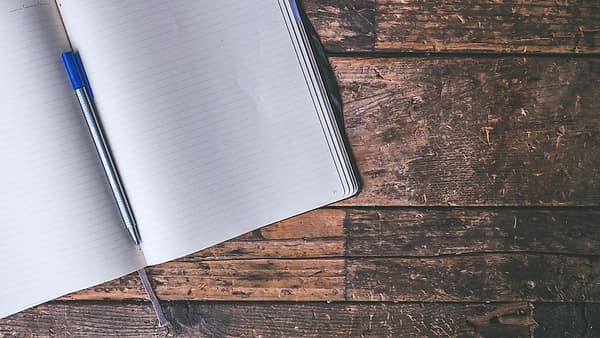 An open journal on a plain surface with a pen resting in the fold between its pages