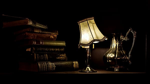 A lamp lit beside a small stack of books on a desk in the evening