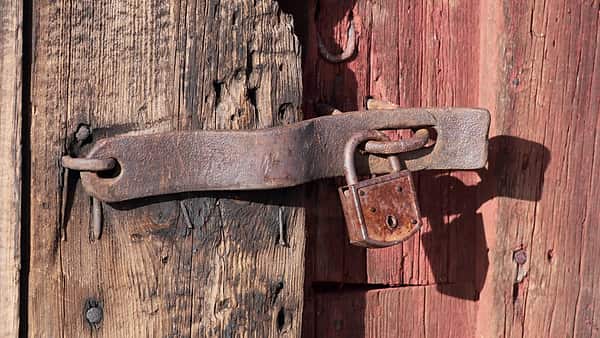 A heavy padlock hanging from the door of an old timber storehouse in daylight