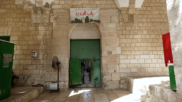 A closed iron gate set into a stone wall, its bars throwing shadows across the ground