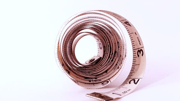 A white cloth measuring tape coiled into a loose spiral on a plain background