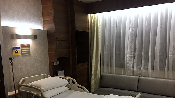 A modern hospital room with an adjustable bed, a sofa and soft ambient lighting