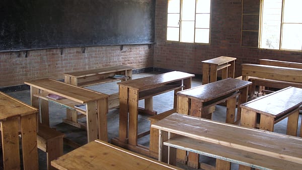 An empty classroom with rows of desks and chairs and bare walls behind them