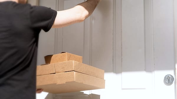 A courier standing at a front door with a parcel in hand, waiting for an answer