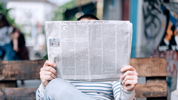 A person holding an open newspaper up in front of them, the printed columns facing out
