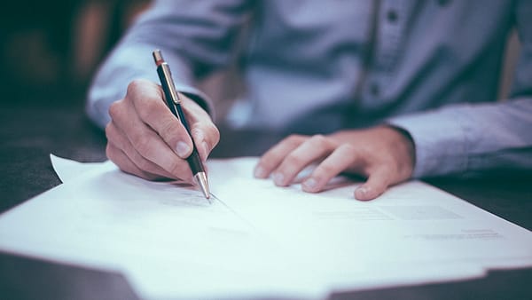 A printed page on a desk with a pen laid across the line where a signature belongs