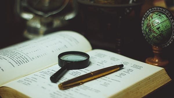 A magnifying glass resting on an open book beside a small desk globe