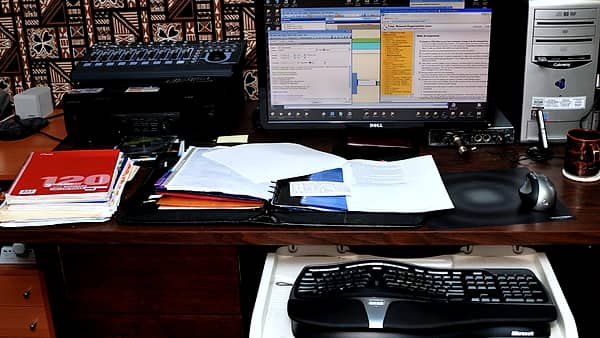 A working desk with an open ring binder, loose papers, a monitor and a keyboard