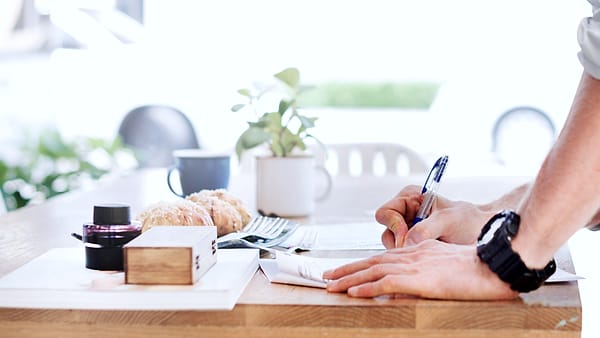 Somebody standing at a desk writing on a sheet of paper by hand