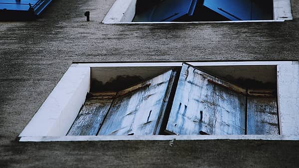 Closed blue wooden window shutters on a weathered plastered wall in flat daylight