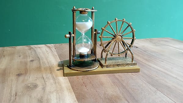 A glass hourglass standing upright with the sand collected in its lower chamber