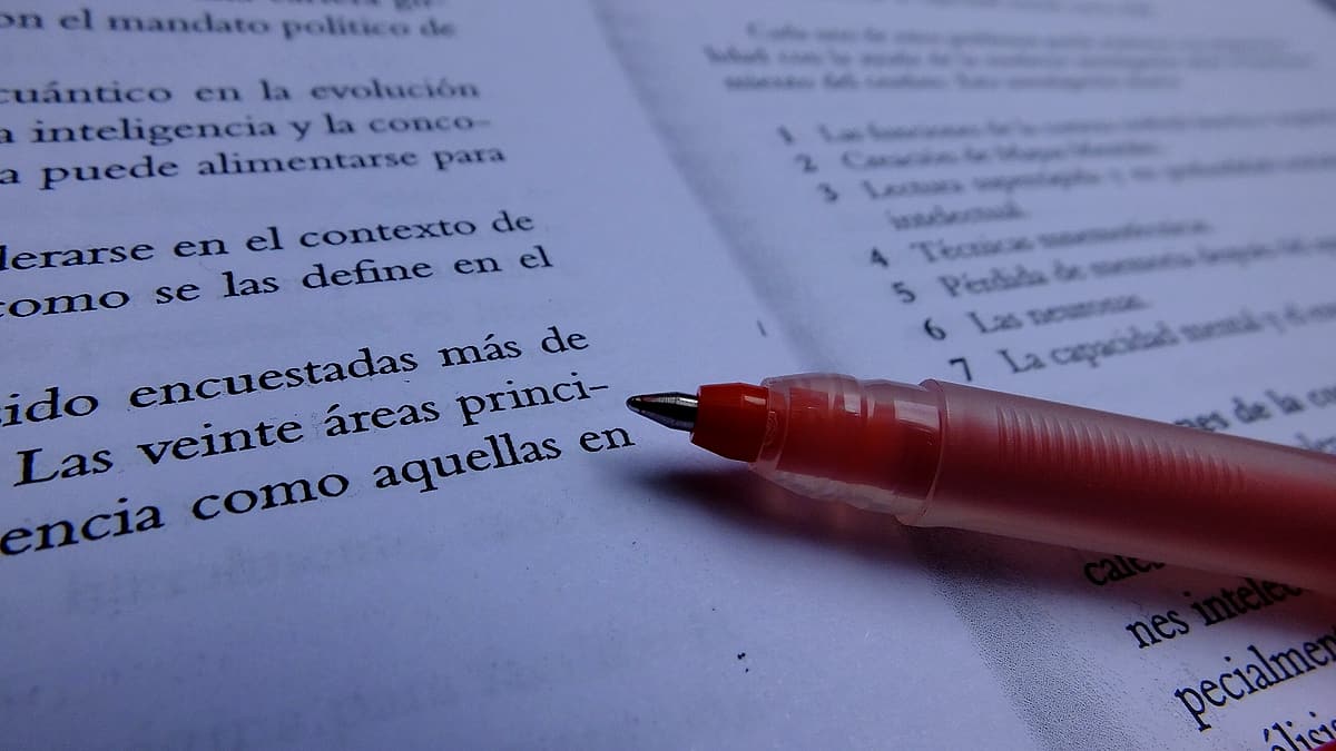 A red pen resting on a printed page that has been marked up with handwritten corrections