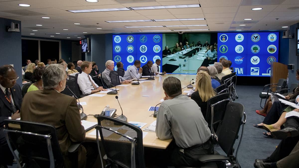 A video conference room with screens at one end and seating facing them