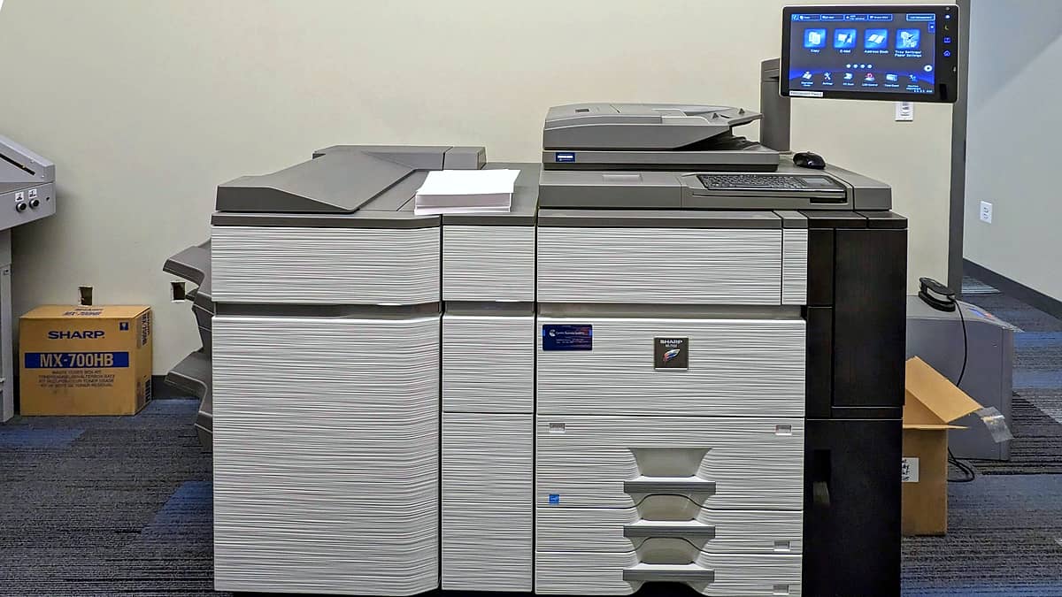 A large office photocopier standing against a wall with its output tray open