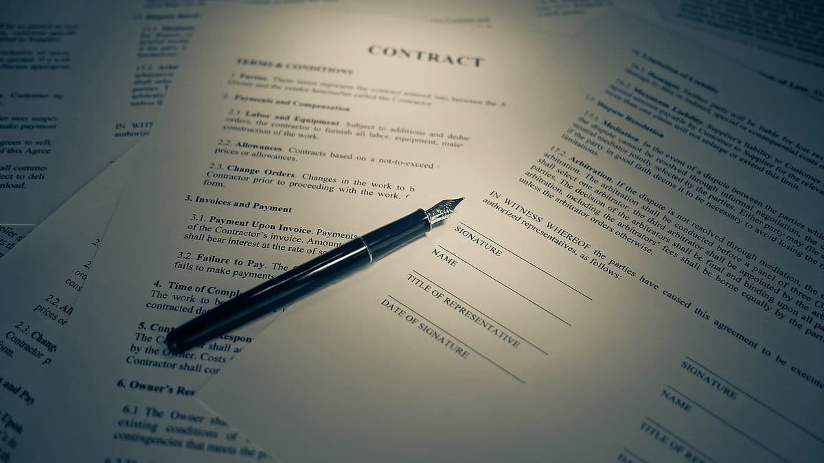 A printed contract lying on a desk with a pen resting across the signature block