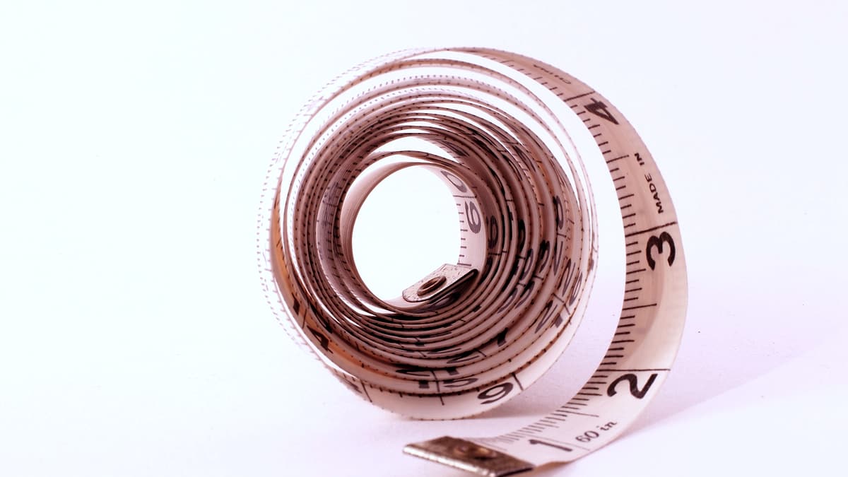 A white cloth measuring tape coiled into a loose spiral on a plain background