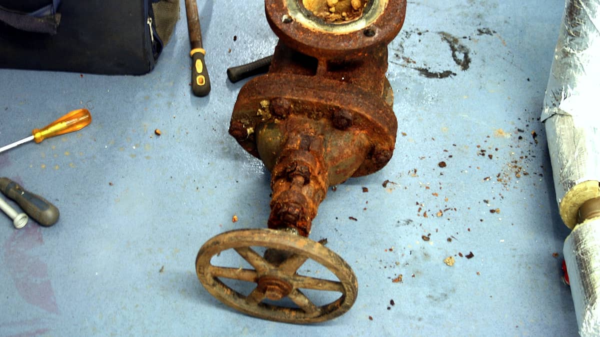 A corroded metal valve and its pipework fitted against a painted industrial wall
