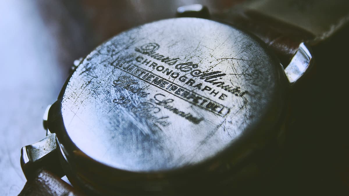 A scuffed vintage wristwatch lying face up on a plain flat surface