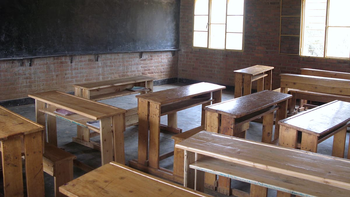 An empty classroom with rows of desks and chairs and bare walls behind them