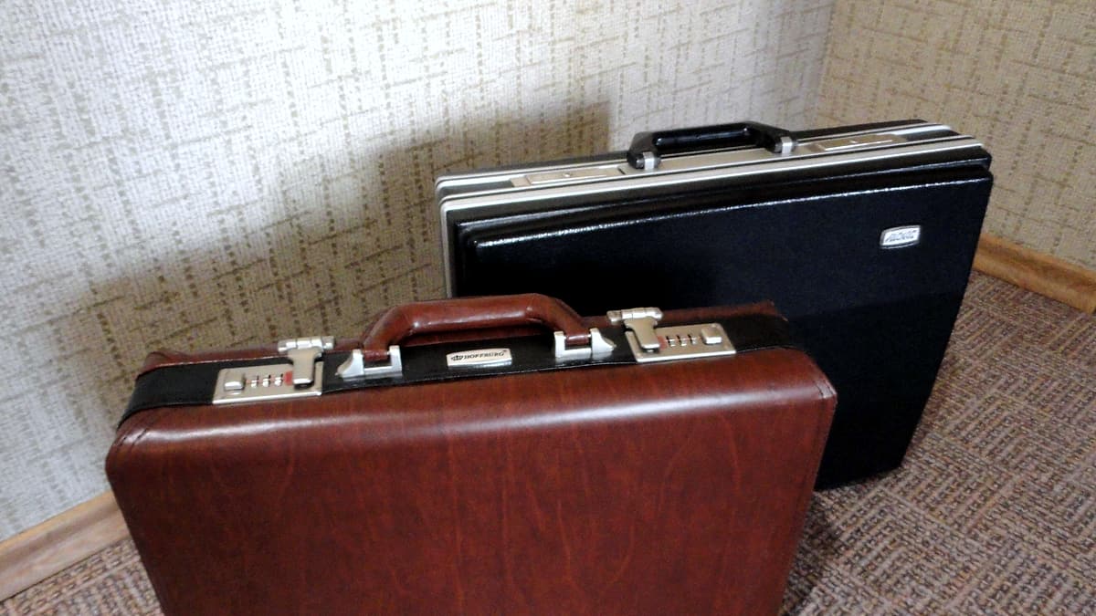 Two hard-sided briefcases standing closed against a wall, one leather and one dark