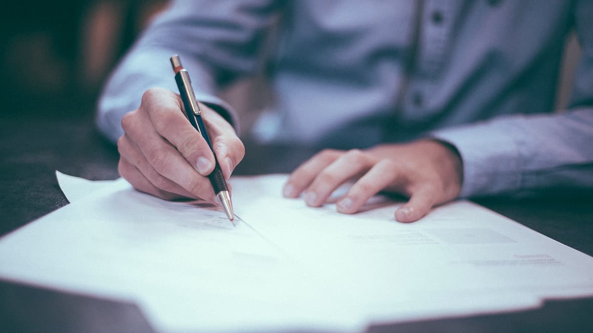 A printed page on a desk with a pen laid across the line where a signature belongs