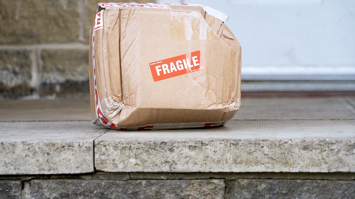 A crushed cardboard parcel left on a doorstep beside the frame of a closed door