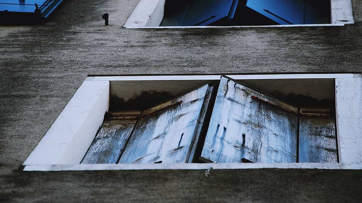 Closed blue wooden window shutters on a weathered plastered wall in flat daylight